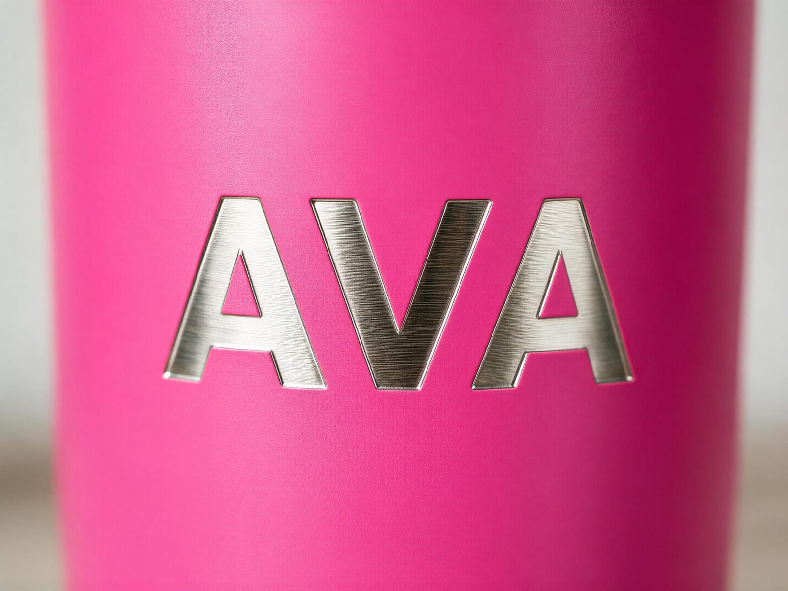 Macro of a name engraved into a pink powder-coated tumbler, the laser revealing bare steel